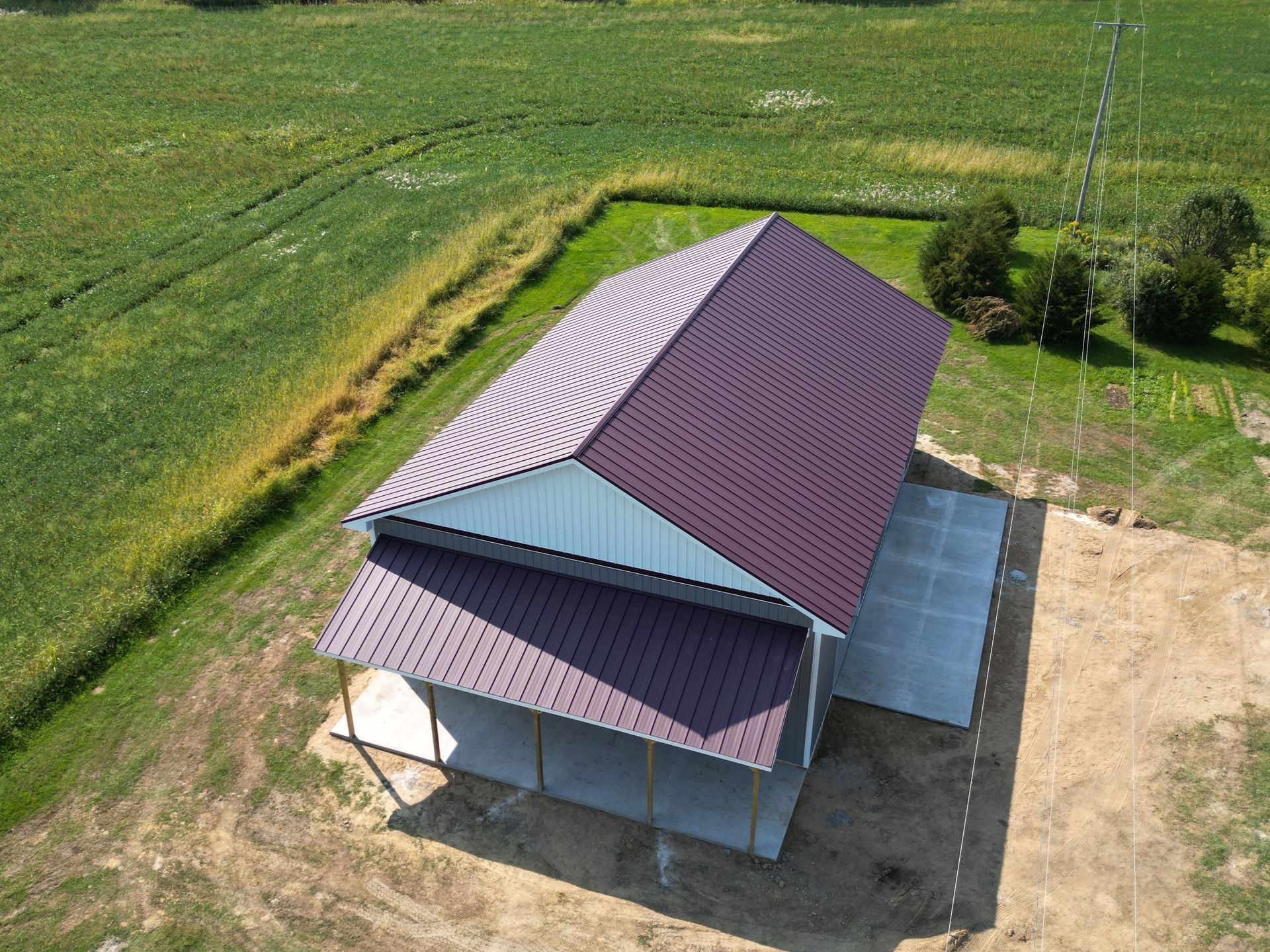 A burgundy-roofed pole barn with a concrete patio sits on a green field.