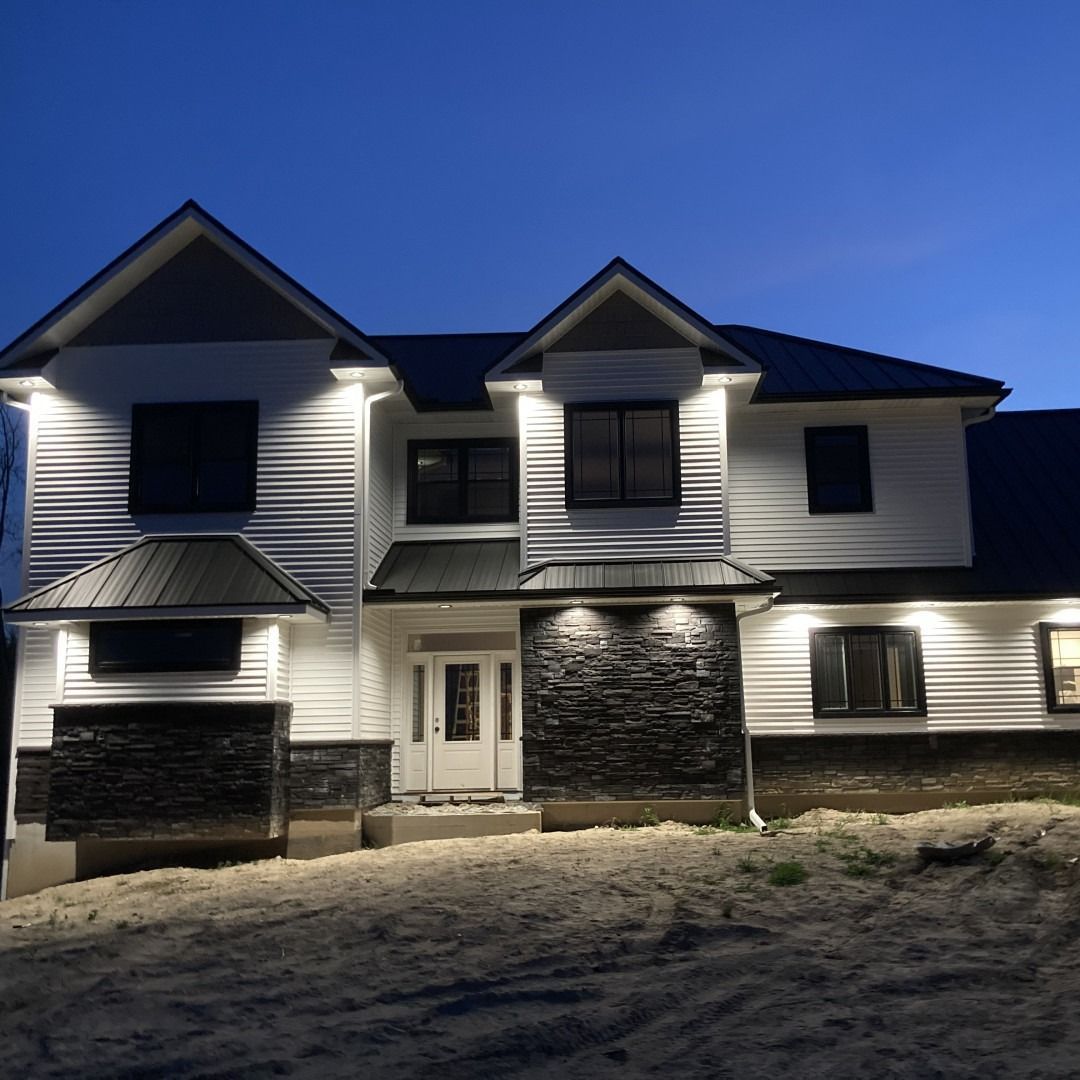 Two-story white house with black trim at dusk, illuminated by lights. Dark blue sky.