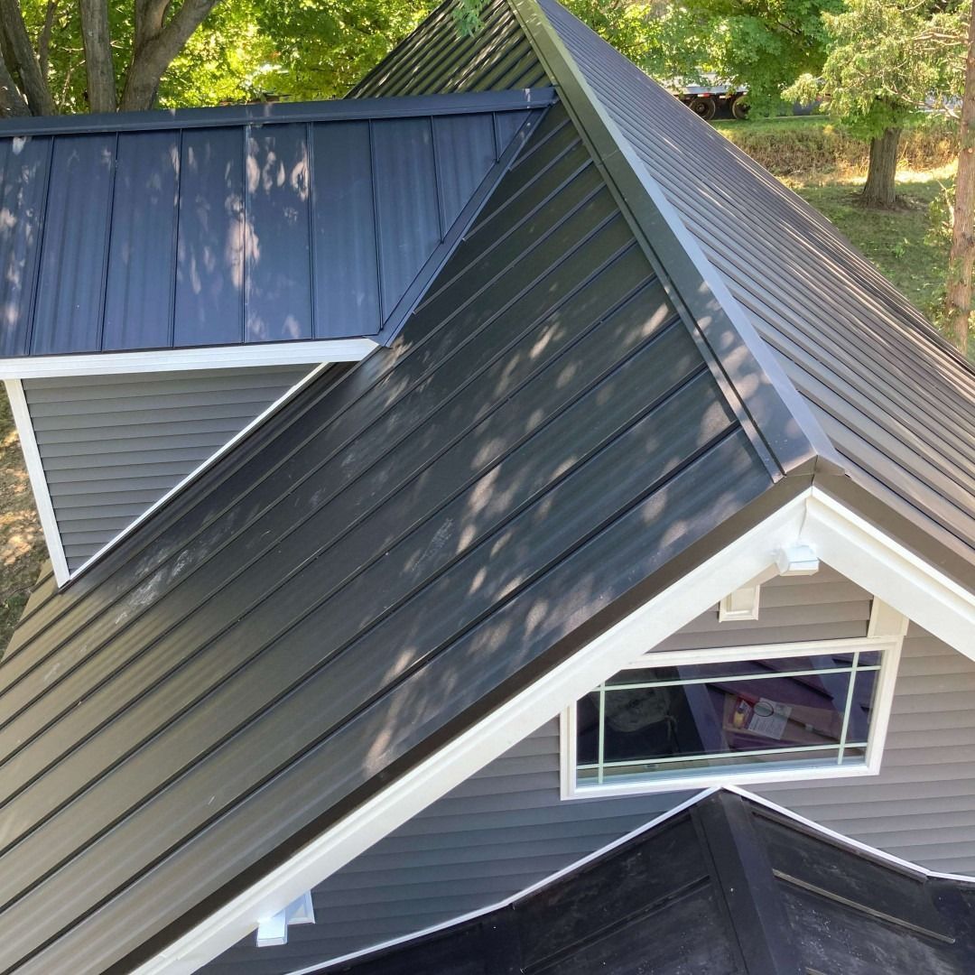 Black metal roof on a gray house with white trim. Window visible.