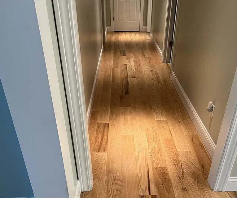 Wooden hallway with light brown floorboards, tan walls, and white trim.