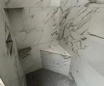 Tiled shower with marble-like pattern and built-in corner seat and shelf. Partially constructed, interior view.
