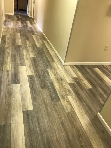 Hallway with wood-look flooring in shades of gray and white, beige walls, and white baseboards.