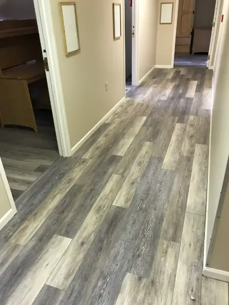 Hallway with gray and beige wood-look flooring and beige walls. White door frames. Three framed art pieces on the wall.