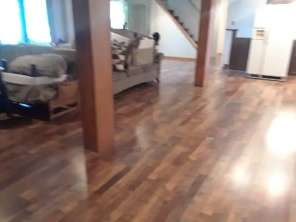 Wooden-floored interior with brown support beams and a sofa. Stairs and a refrigerator are visible in the background.