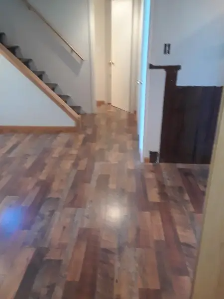 Hardwood floors in a hallway with stairs on the left and a door in the distance.