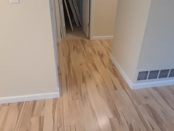 Light wood floor hallway with beige walls and white trim. Air vent on right wall. Open doorway.