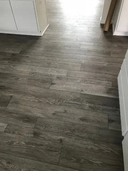 Gray wood-look plank flooring in a room, contrasting with white cabinets.