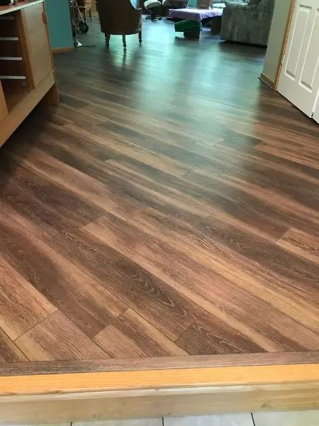 Diagonal wood-look flooring, light and dark brown planks, leading to a door.