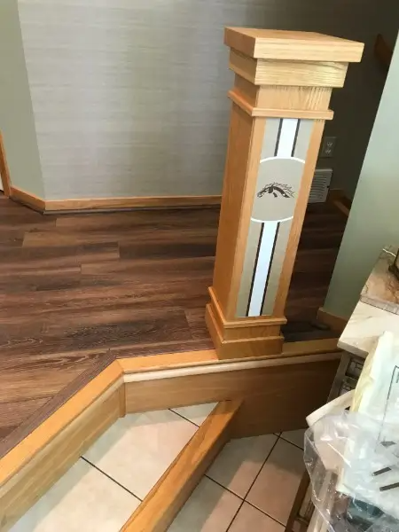 Wooden newel post with a decorative stripe and team logo, near a staircase with wood flooring.