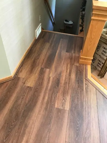 Wood-look flooring in a hallway with stairs leading down. Light beige walls and a wood banister.