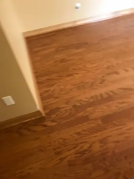 Wooden floor in a room with light tan walls, a white electrical outlet, and a door frame.