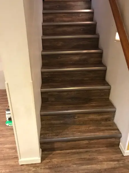 Wooden staircase with metal edges, indoors. Brown and beige tones, leading upwards.