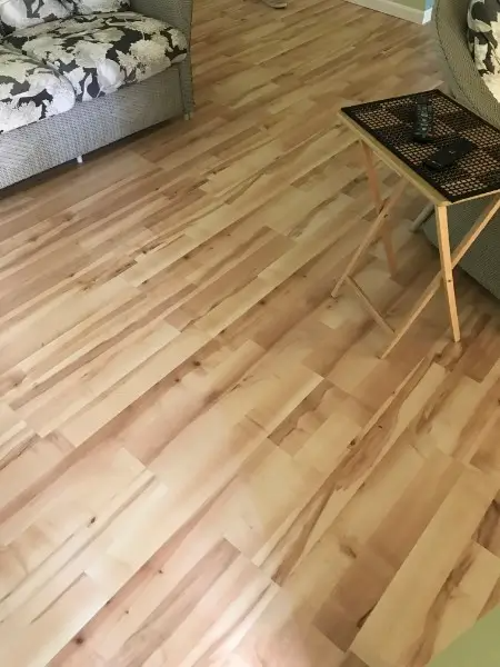 Light wood flooring in a room with a patterned couch and a small table.