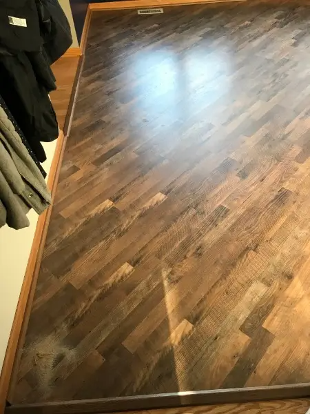 Herringbone pattern hardwood floor, dark brown with light highlights. Coats hanging on the left side.