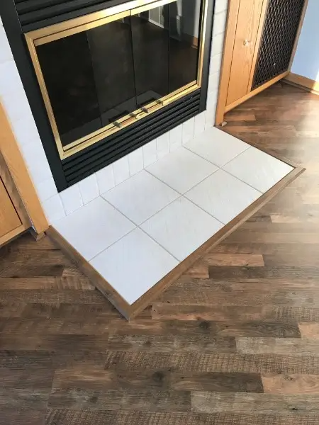 Fireplace with white tile hearth, framed by wood flooring.