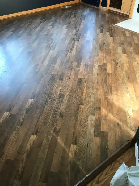 Dark wood-look flooring fills a room, reflecting light. The floor is made of planks in varying shades of brown.