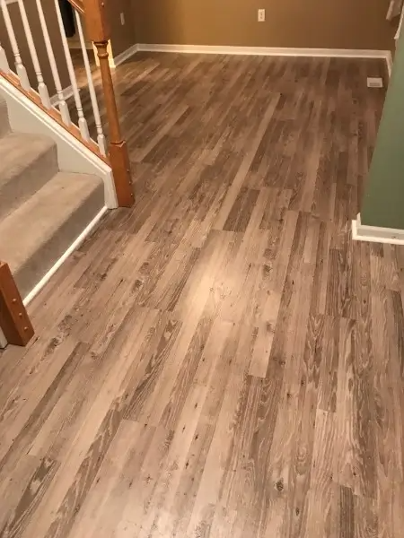 Wood-look flooring in a room, with carpeted stairs and a tan wall visible.