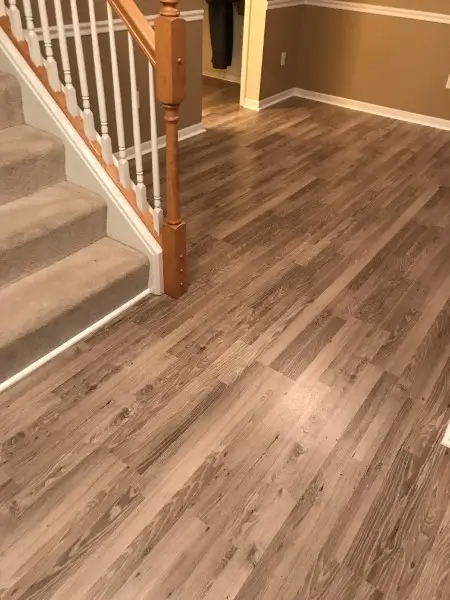 Wooden-look flooring next to a carpeted staircase and a wooden banister in a house.