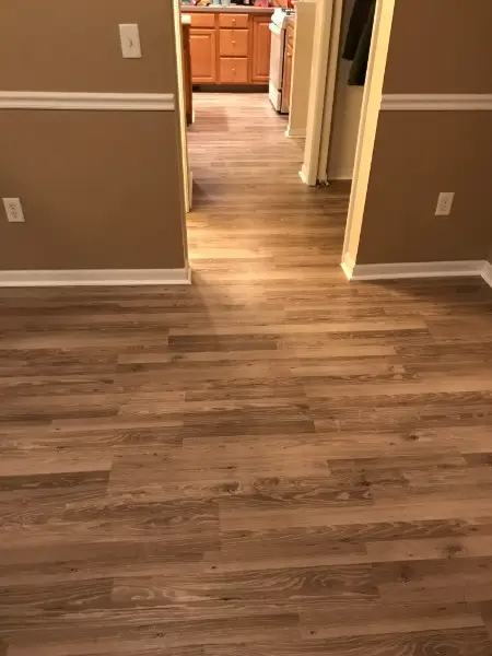 Laminate flooring in entryway with tan walls, white trim, and a glimpse of the kitchen.