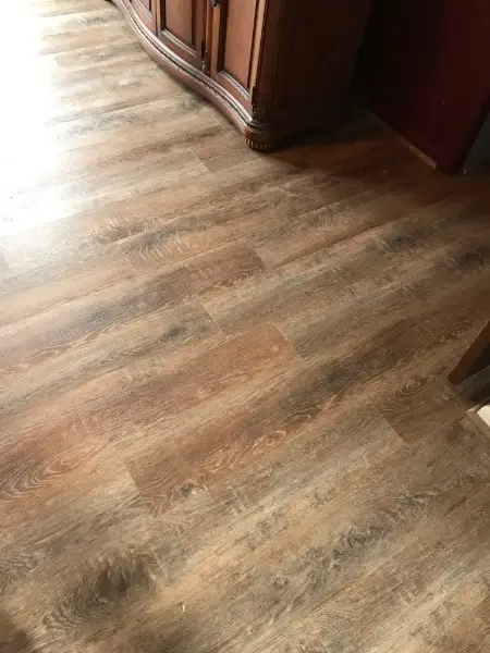 Wooden-look flooring with varying shades of brown and gray. A dark wooden cabinet is partially visible in the background.