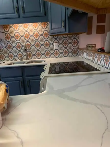 Kitchen with blue cabinets, patterned backsplash, and white countertop with a cooktop.