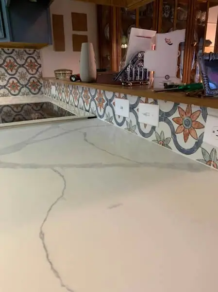 Kitchen counter with floral tile backsplash, quartz countertop, and electrical outlets.