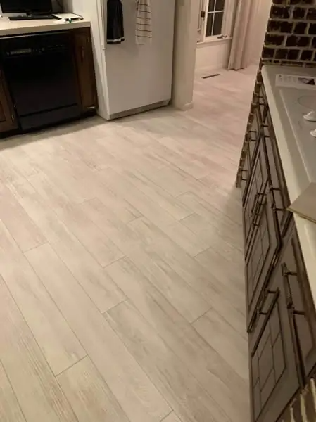 Light wood-look flooring in a kitchen with dark cabinetry and black appliances.