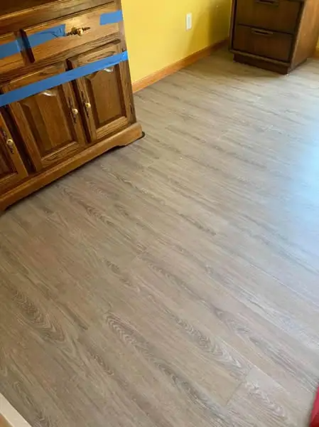 Wooden cabinet next to wood-look flooring. Yellow wall in background.