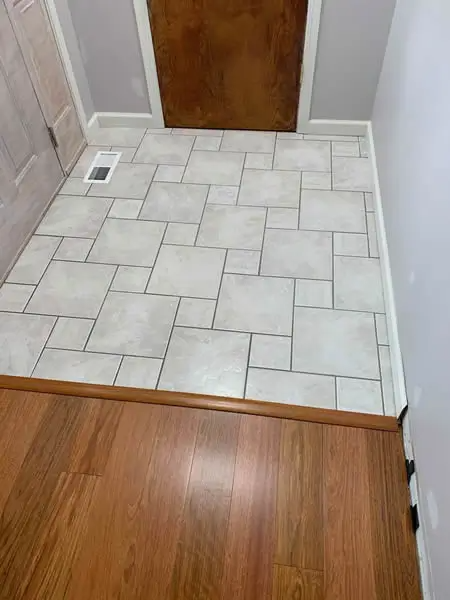 Entryway with wood-look laminate floor and tile flooring leading to a brown door.