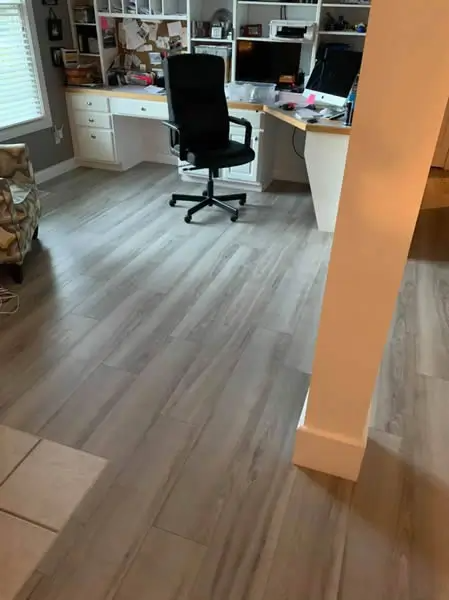 Gray wood-look flooring in home office with white desk, shelves, and black office chair.