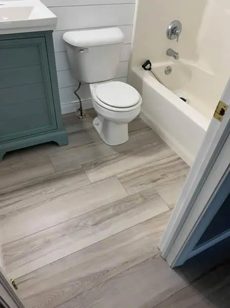 Bathroom with wood-look flooring, a white toilet, blue vanity, and a white bathtub.