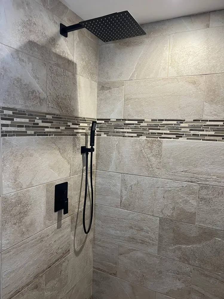 Shower with beige tiled walls, a dark square showerhead, and black fixtures.