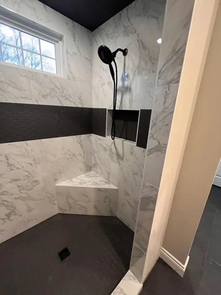 Modern shower with white marble walls, dark floor, built-in bench, and black fixtures.