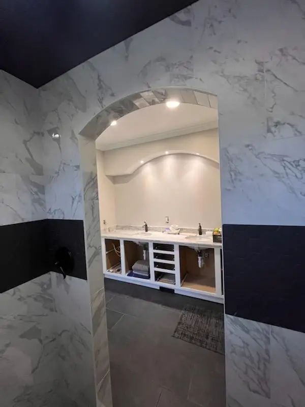Bathroom with marble tile walls, a black accent, and an arched entry to a vanity area.