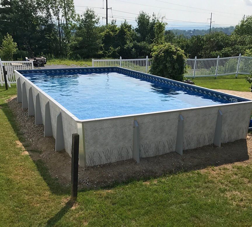 A large swimming pool is surrounded by grass and a white fence