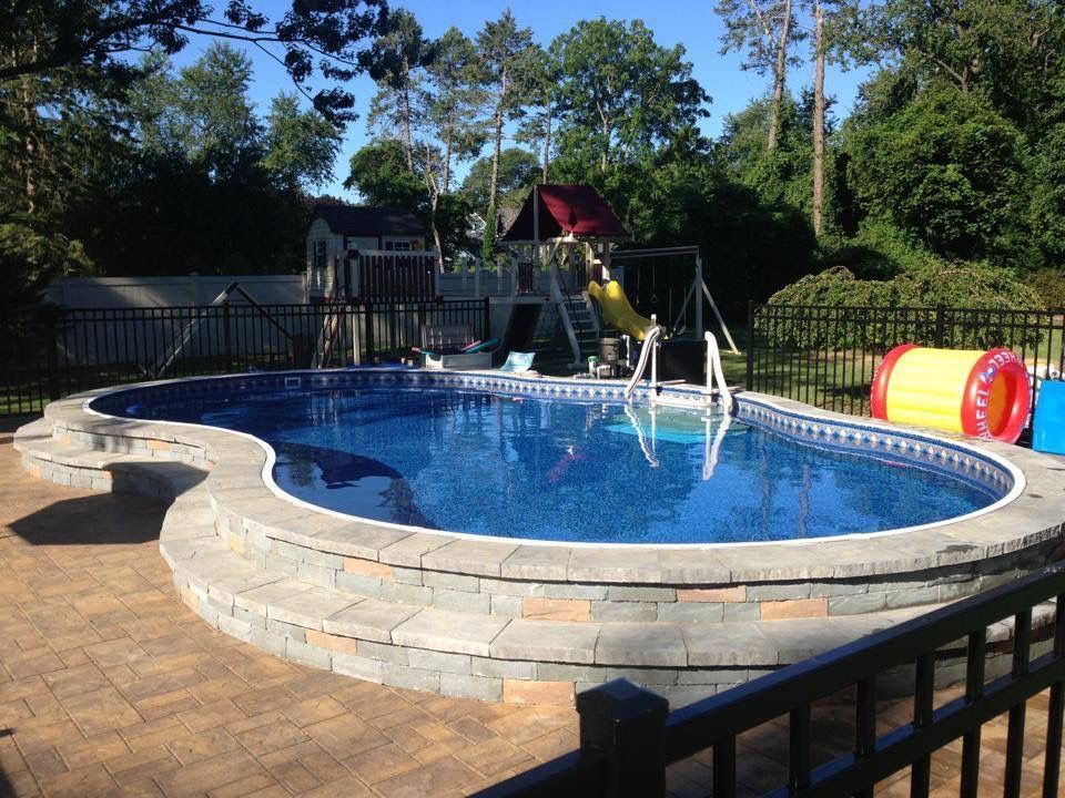 A large swimming pool is surrounded by a fence and a playground.