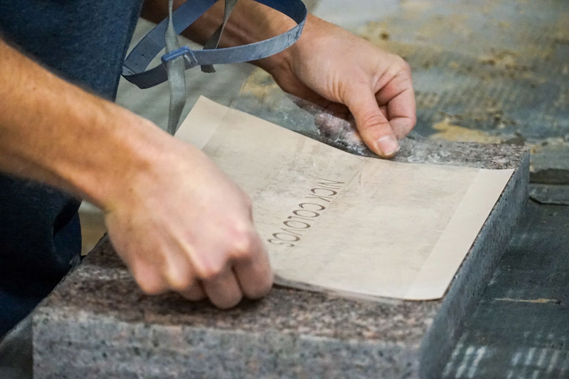 Person peeling stencil from stone surface, revealing etched text.
