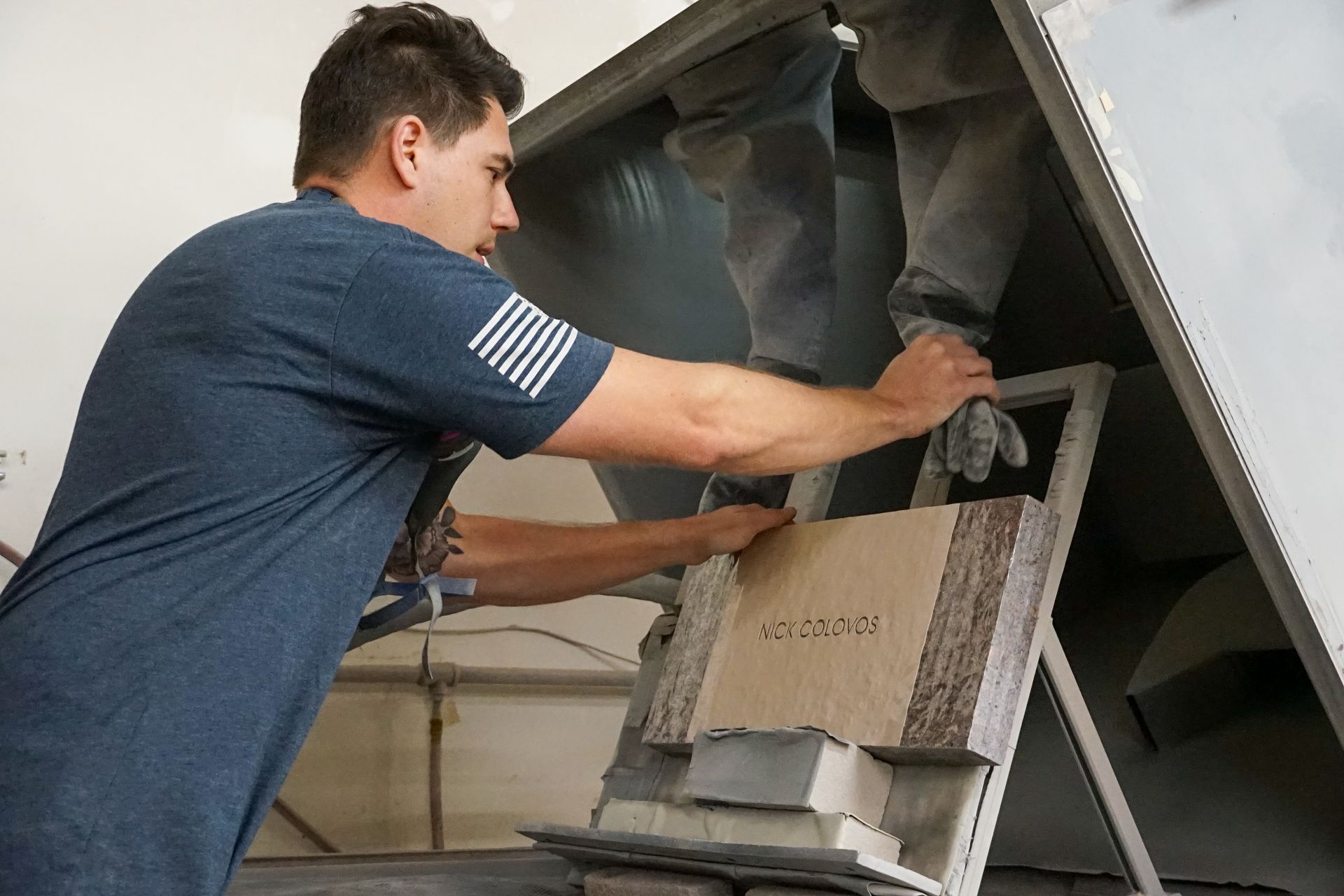 Man in blue shirt working on machinery, holding a block.