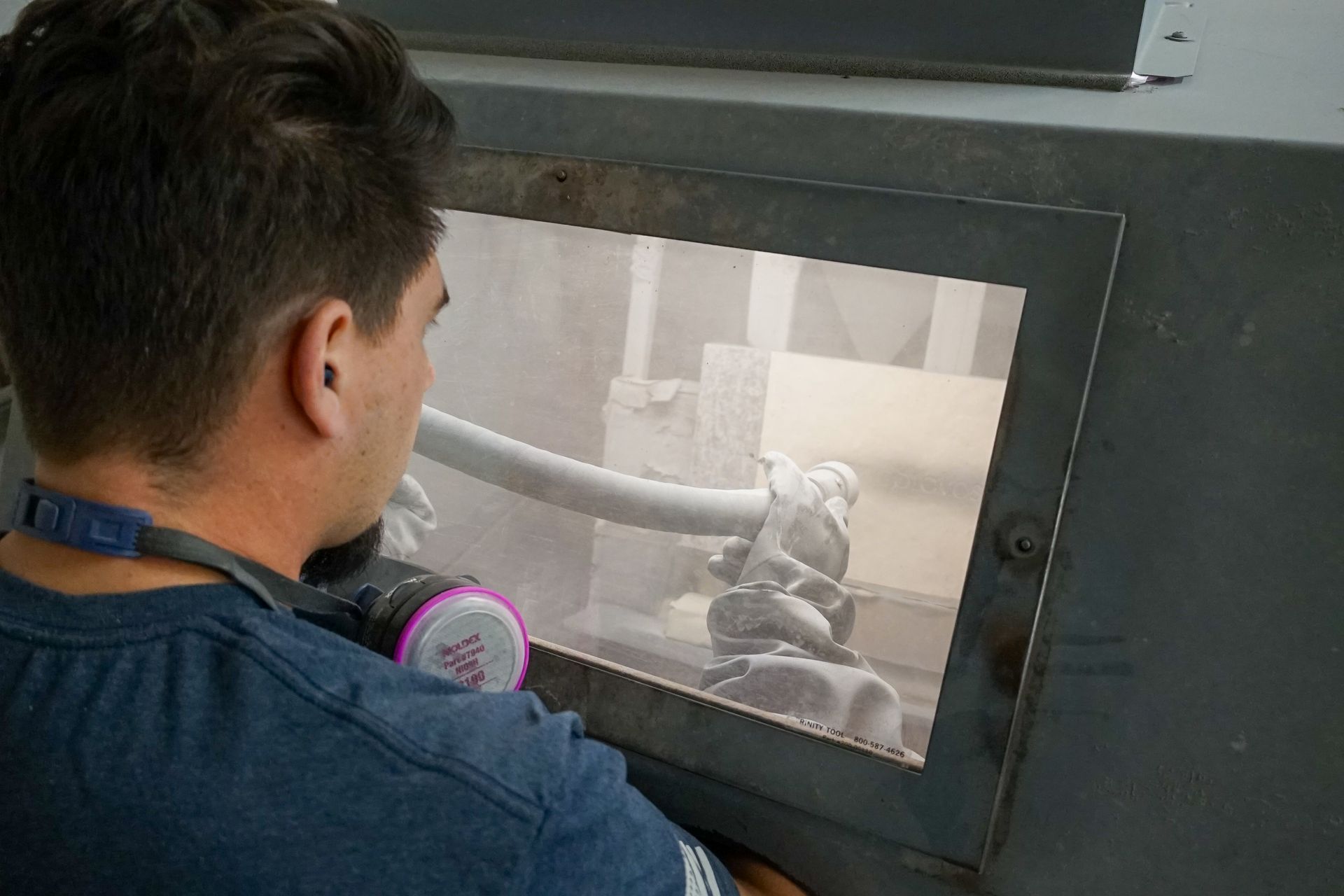 Person using a sandblasting machine with protective gear, inside an enclosed booth.