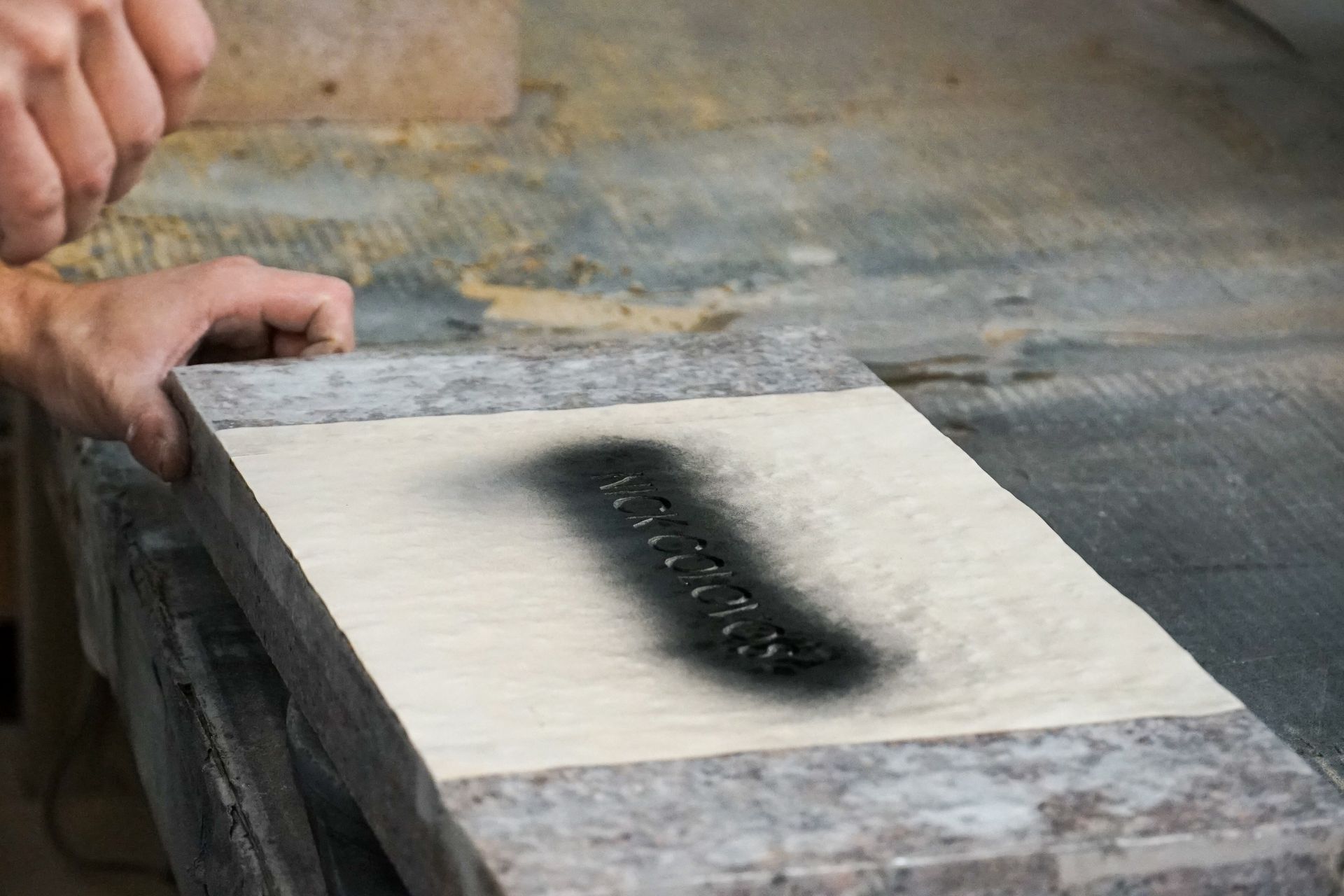 Person spray painting dark text onto a light-colored stone slab.