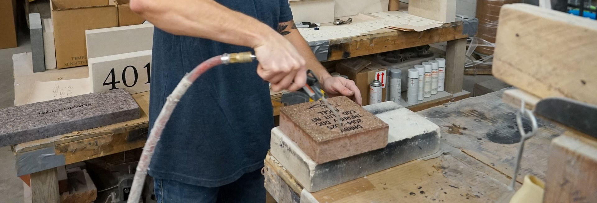 Person spraying a brick with an air hose in a workshop.