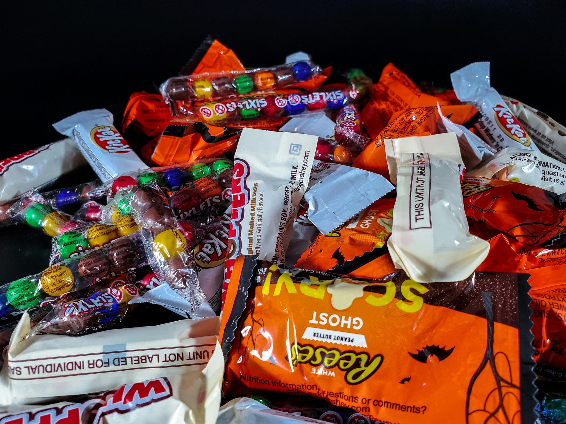 Assorted colorful Halloween candies and chocolate bars piled together on a black background