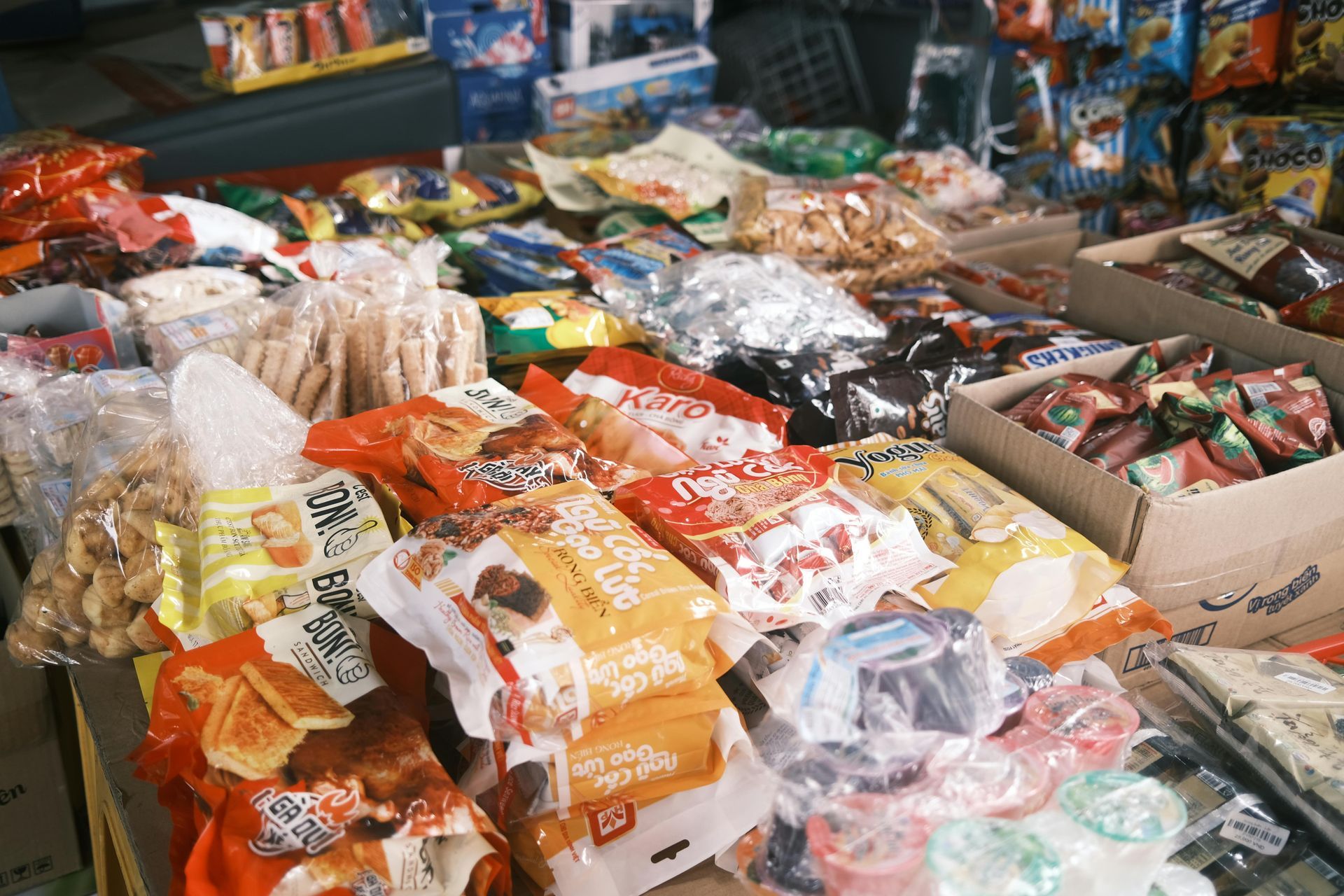 Assorted packaged snacks and sweets piled on a market stall table, with colorful wrappers and bags.