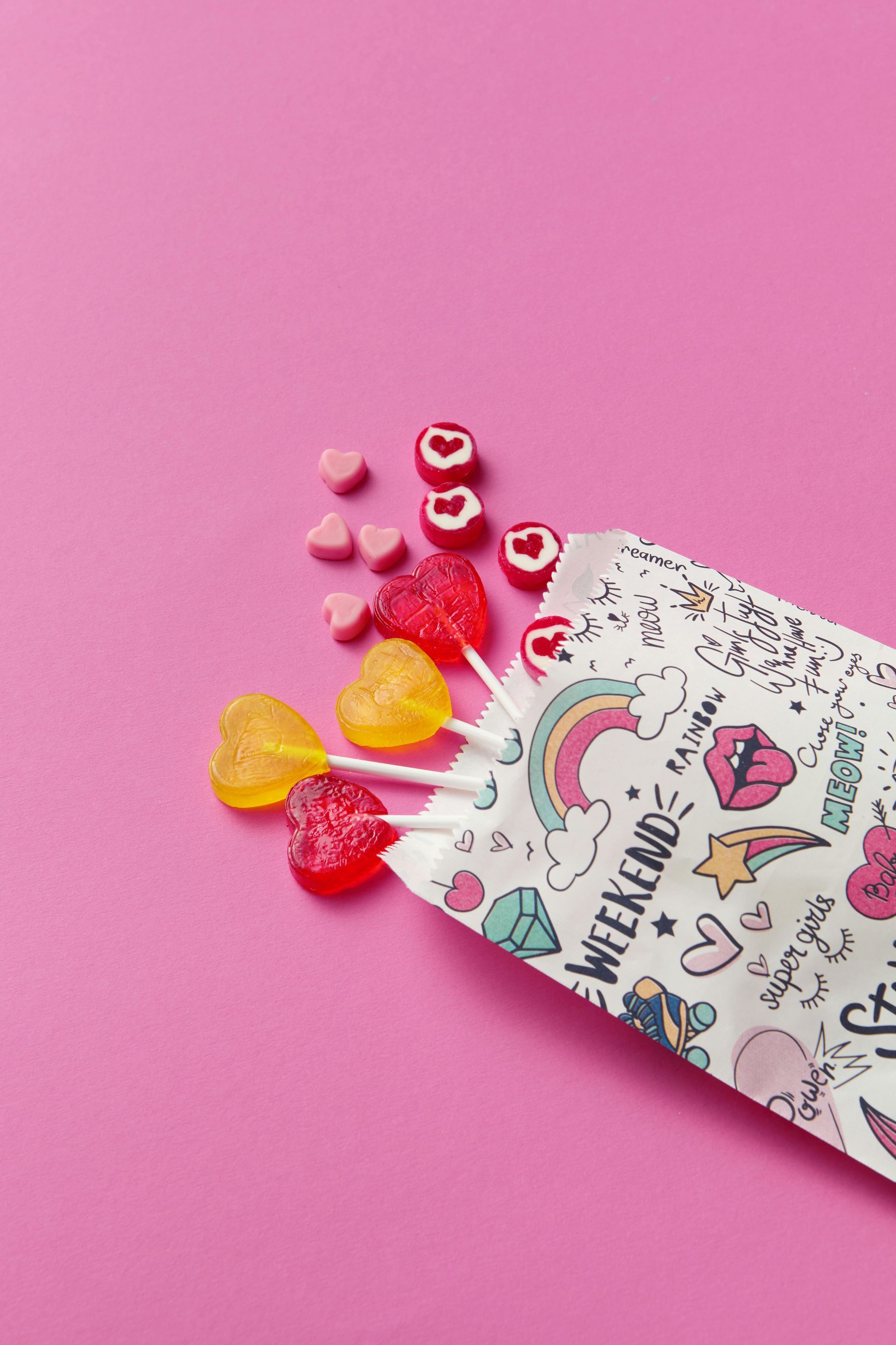 Heart-shaped candies spilling from a decorated packet on a pink background