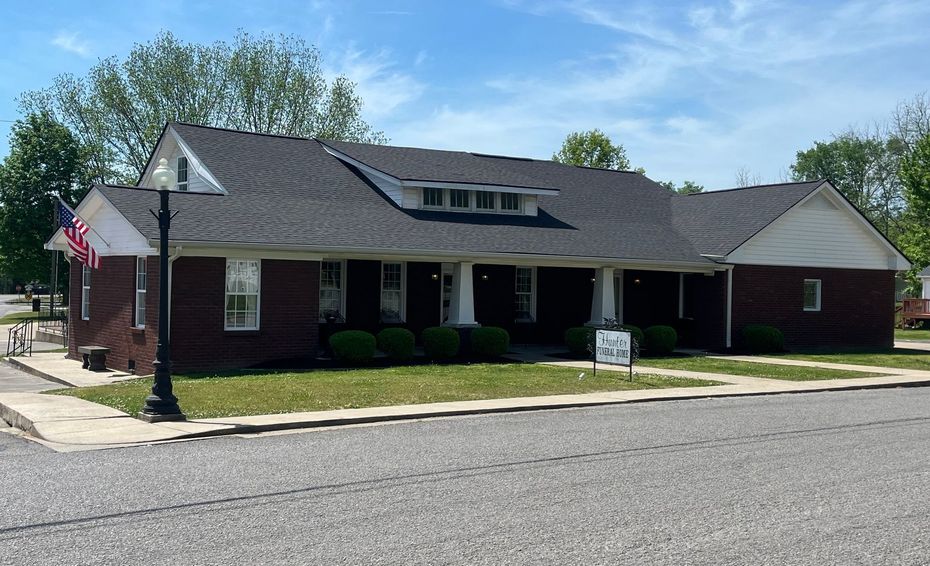 Brick building with a covered porch, American flag, and manicured lawn on a sunny day