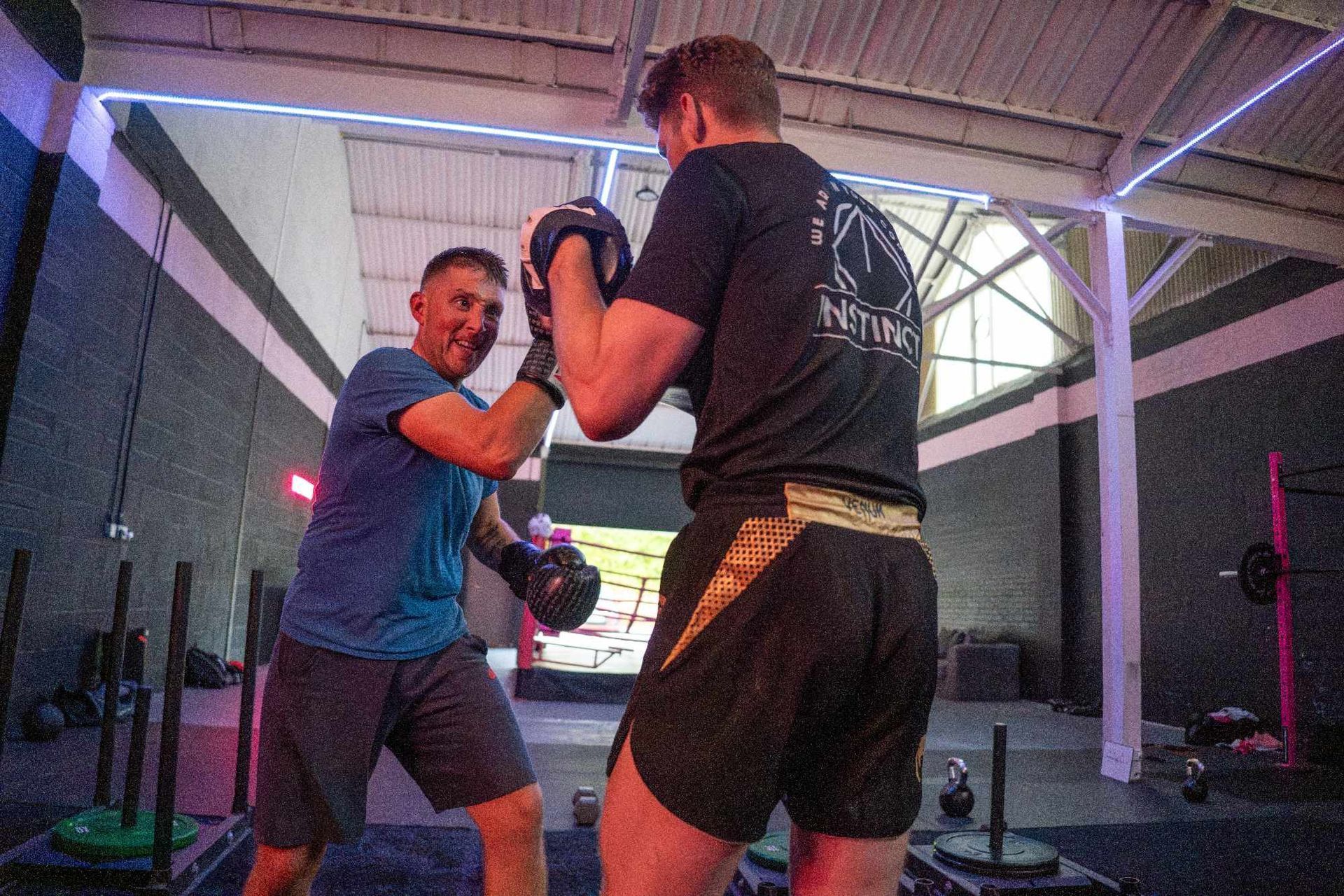 Two people boxing indoors, one holding pads and the other throwing punches.