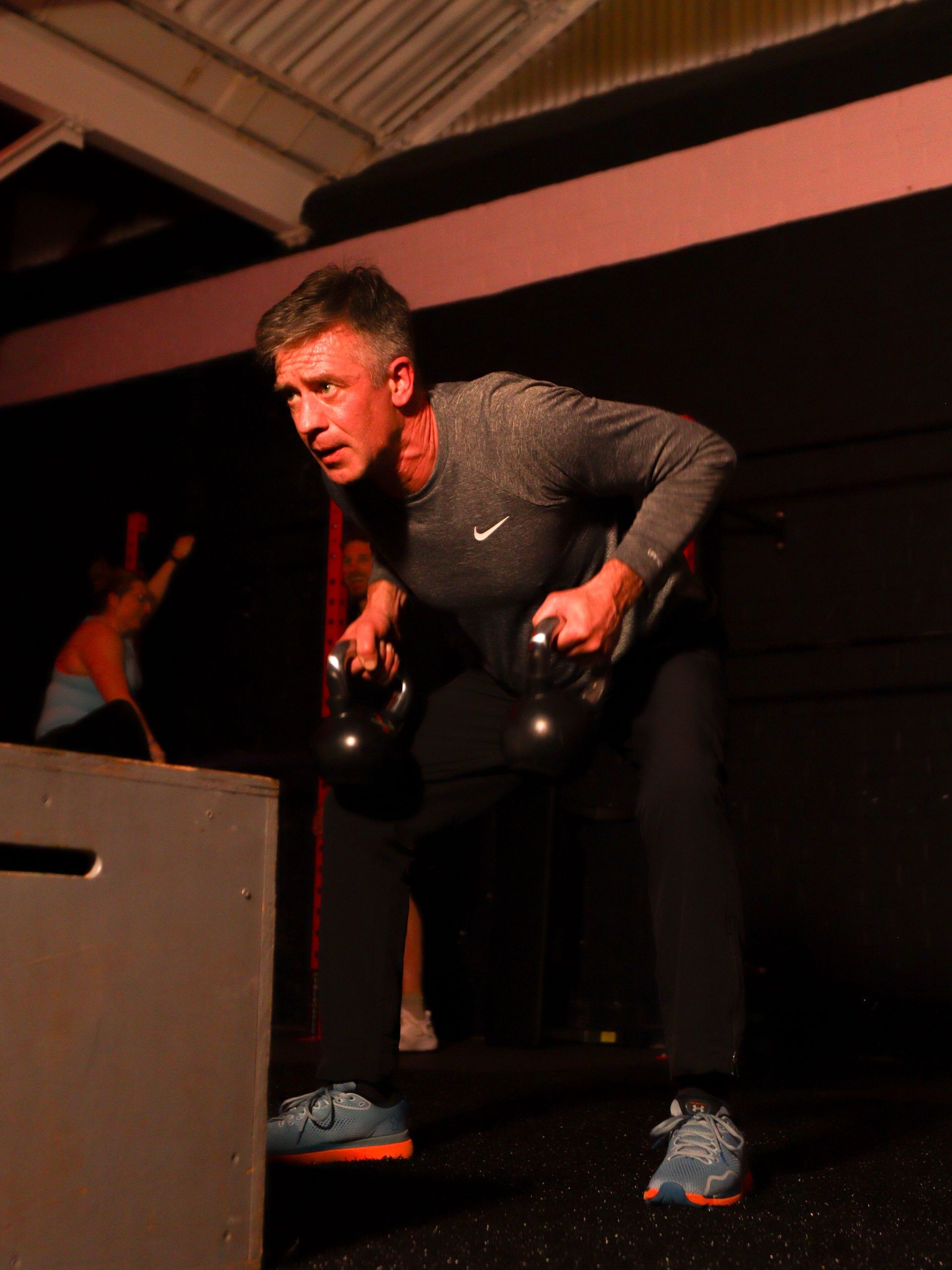 Man in dark workout clothes lifting kettlebells in a dim gym