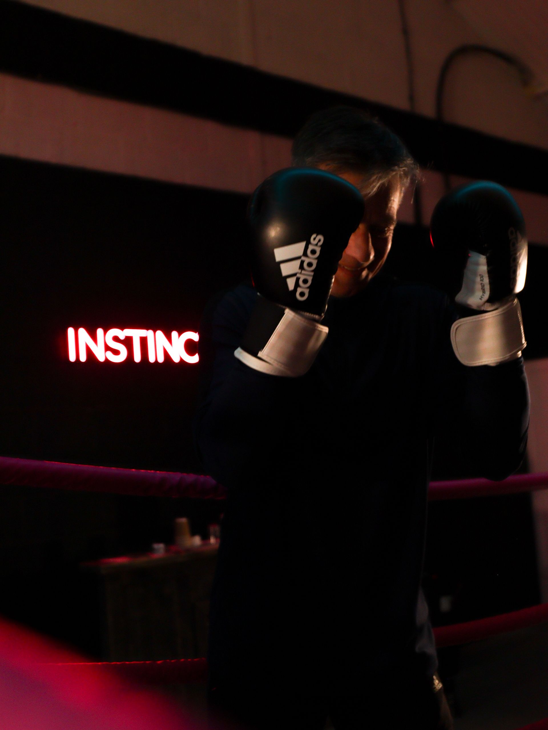 Boxer in black gloves in a dimly lit ring beside a red neon “INSTINCT” sign