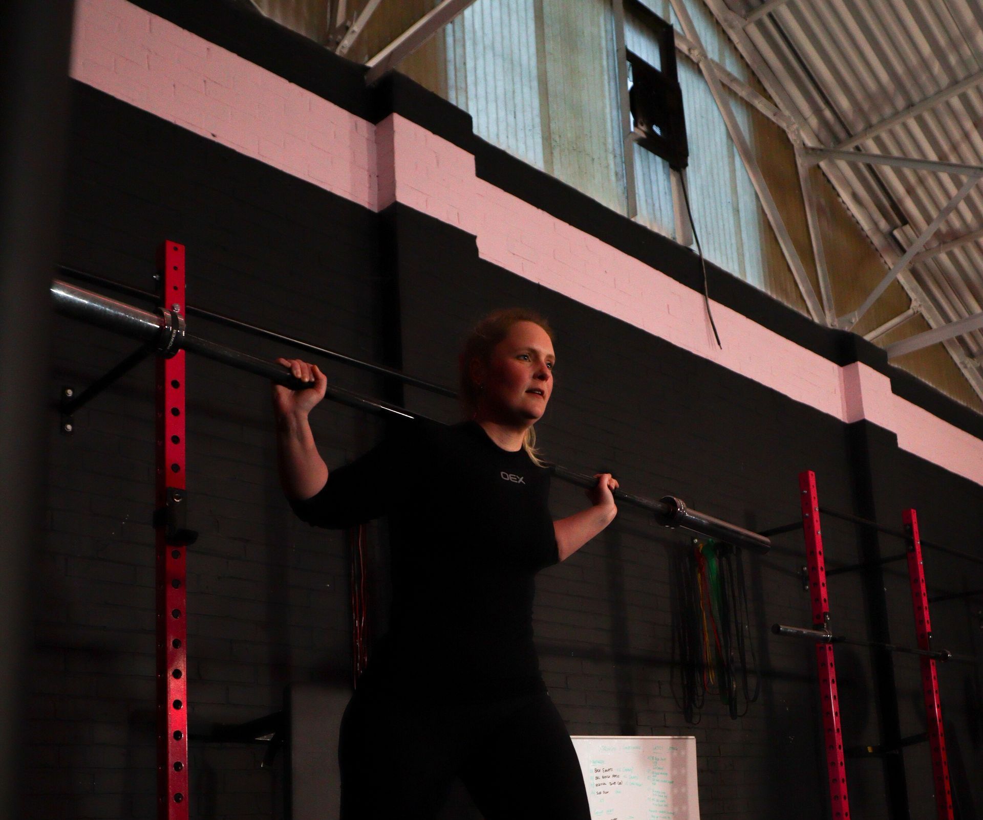 Person doing a squat with a barbell in a gym, black walls and red rack behind them.