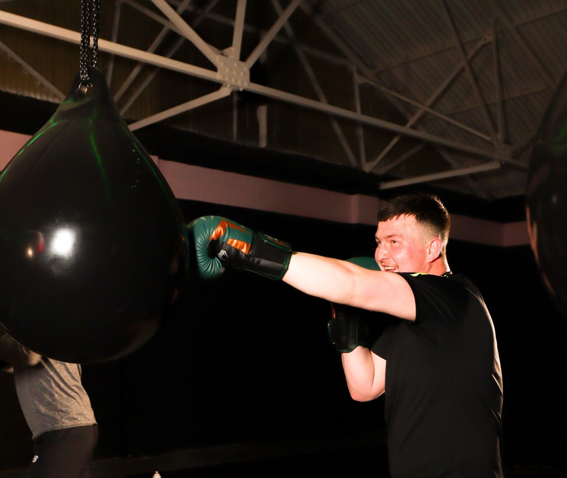 Man in boxing gloves punches a black speed bag in a gym, arm extended